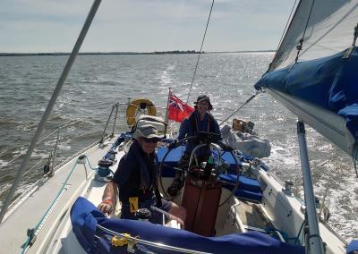 Photo taken looking aft on a Moody sailing boat, slightly heeled on a nice day. Skipper is standing at the wheel.